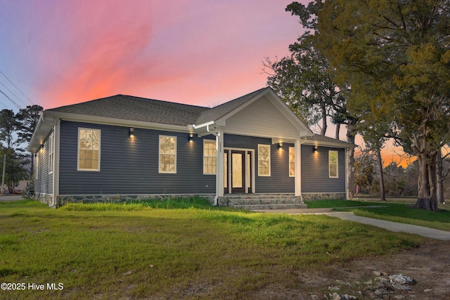 view of front of house with a shingled roof, covered porch, and a front lawn