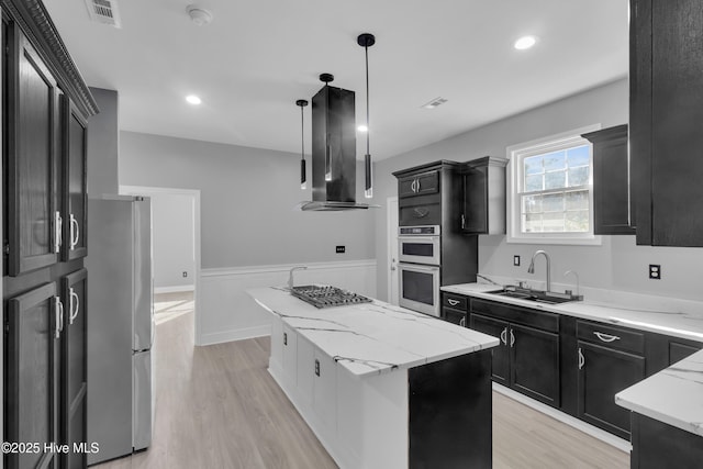 kitchen featuring visible vents, a kitchen island, appliances with stainless steel finishes, ventilation hood, and a sink