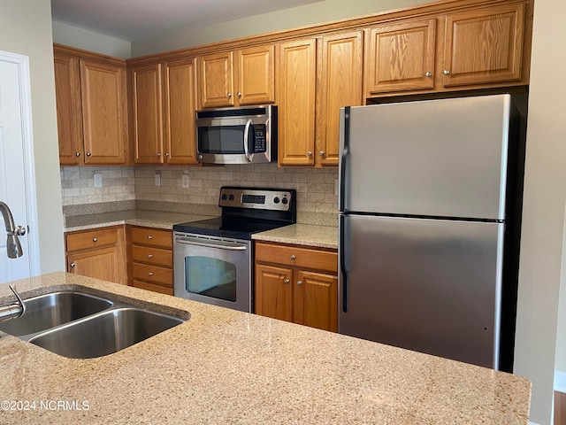 kitchen with decorative backsplash, stainless steel appliances, light stone countertops, and sink