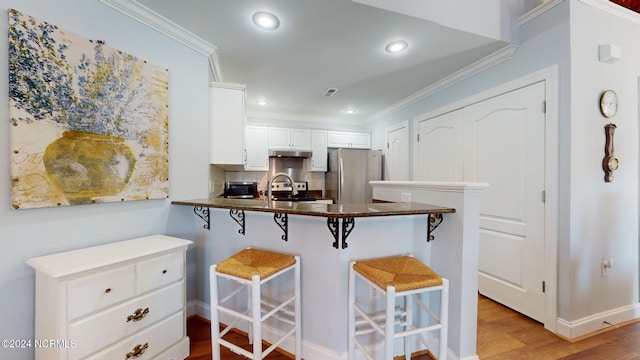 kitchen with white cabinets, tasteful backsplash, hardwood / wood-style floors, a breakfast bar area, and appliances with stainless steel finishes