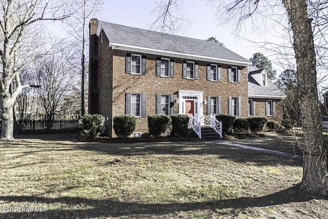 colonial home featuring brick siding, fence, a chimney, and a front lawn