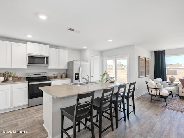 kitchen with light hardwood / wood-style flooring, a breakfast bar area, a kitchen island with sink, white cabinets, and appliances with stainless steel finishes