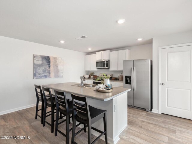 kitchen with white cabinets, light hardwood / wood-style floors, stainless steel appliances, and an island with sink