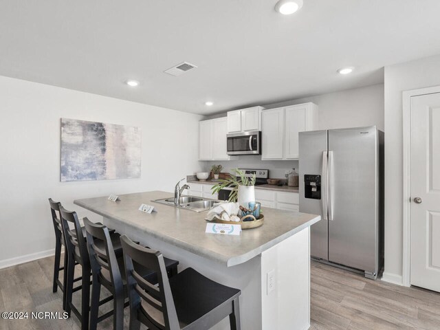 kitchen with white cabinets, a center island with sink, a breakfast bar area, light hardwood / wood-style floors, and stainless steel appliances