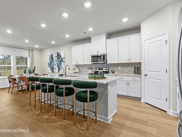 kitchen featuring sink, white cabinetry, stainless steel appliances, light hardwood / wood-style flooring, and a center island with sink