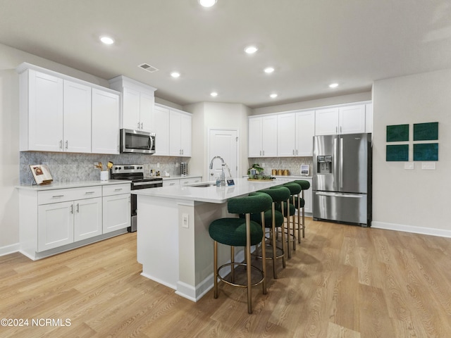 kitchen featuring a breakfast bar area, an island with sink, white cabinets, light wood-type flooring, and appliances with stainless steel finishes