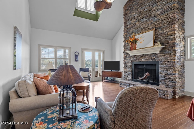 living room with hardwood / wood-style floors, a towering ceiling, ceiling fan, french doors, and a fireplace