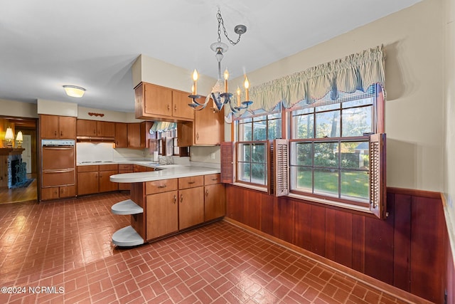 kitchen with wall oven, brick patterned flooring, light countertops, a peninsula, and a wainscoted wall