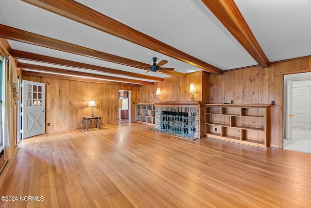 unfurnished living room featuring a fireplace, beamed ceiling, wooden walls, light wood finished floors, and ceiling fan