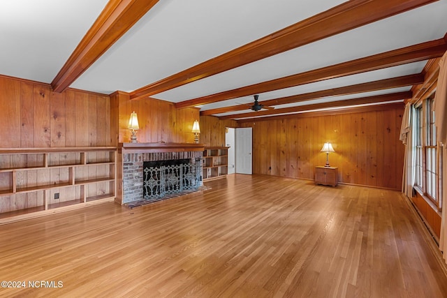 unfurnished living room featuring beamed ceiling, wood walls, a fireplace, a ceiling fan, and light wood-style flooring