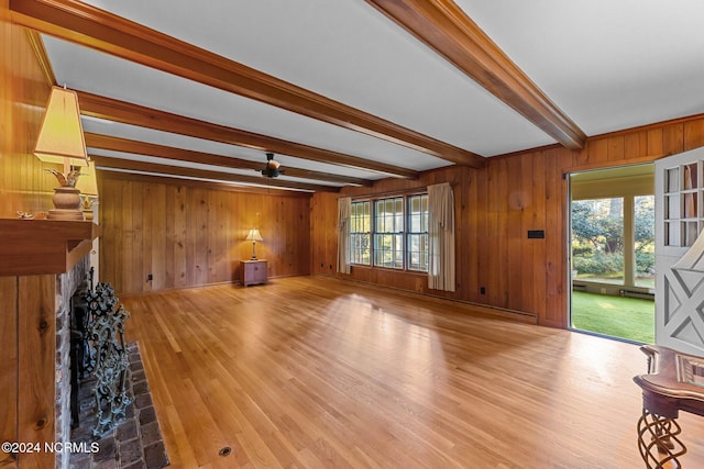 unfurnished living room with wooden walls, beamed ceiling, wood finished floors, and ceiling fan