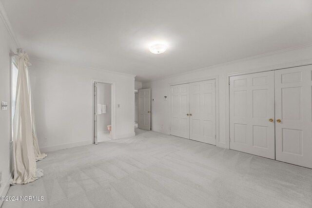 unfurnished bedroom featuring carpet flooring, two closets, crown molding, baseboards, and ensuite bathroom