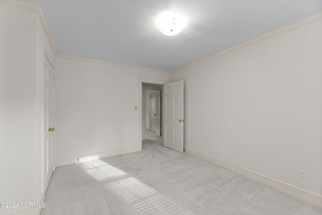 spare room featuring light colored carpet, crown molding, and baseboards