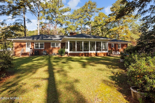 rear view of property with a sunroom, a lawn, and a chimney