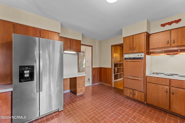 kitchen with stainless steel fridge, oven, a warming drawer, a wainscoted wall, and brown cabinets
