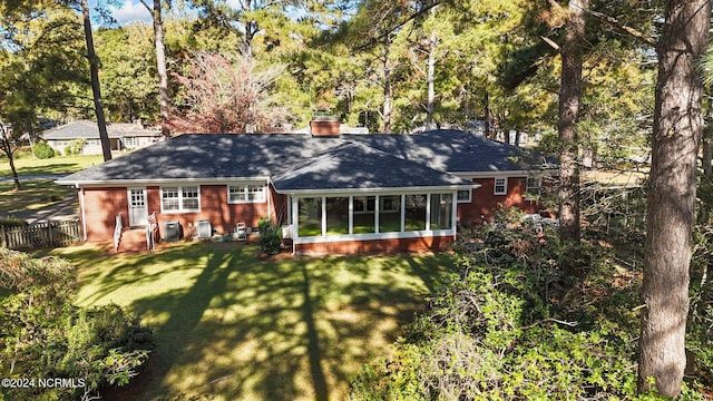rear view of property featuring a sunroom, a chimney, roof with shingles, and brick siding