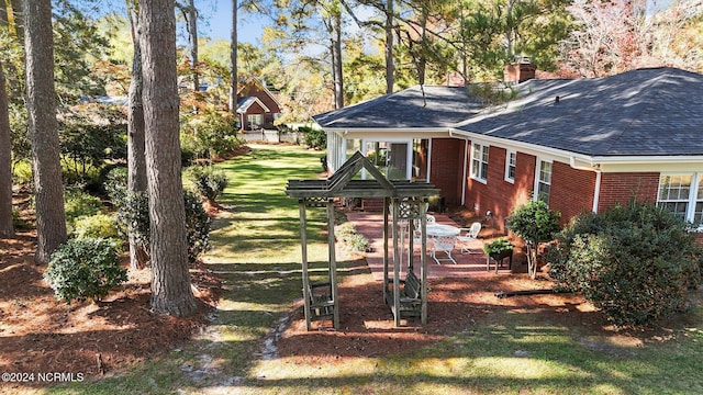 back of house featuring a shingled roof, a chimney, brick siding, a patio area, and a lawn