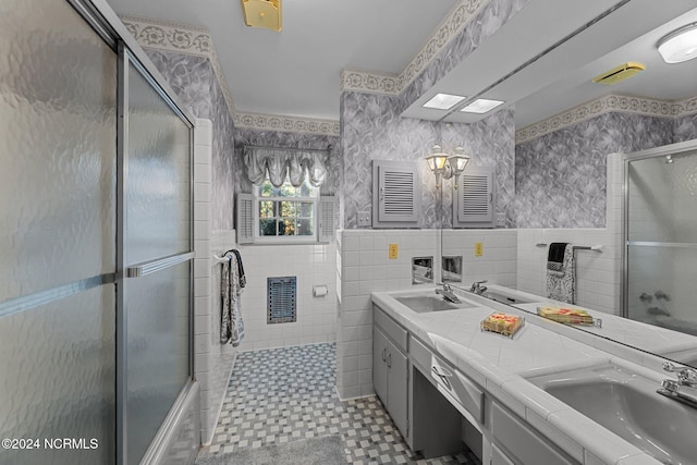 full bathroom with a shower with door, wallpapered walls, tile walls, a wainscoted wall, and double vanity