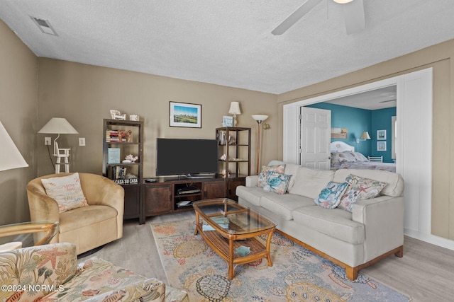 living room with ceiling fan, a textured ceiling, and light hardwood / wood-style floors