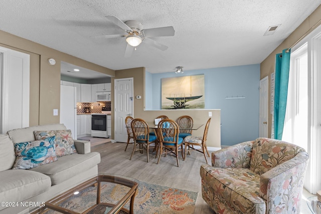 living room with light wood-style flooring, a ceiling fan, and a textured ceiling