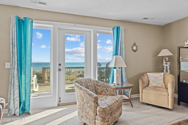 living area with a textured ceiling, a water view, and wood finished floors