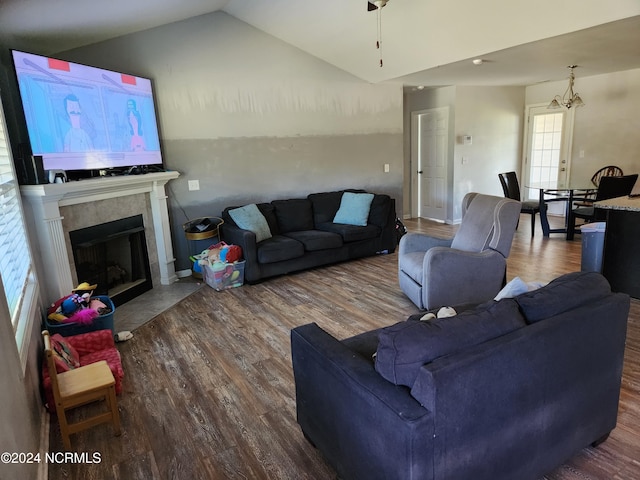 living room with a notable chandelier, hardwood / wood-style floors, a tile fireplace, and vaulted ceiling