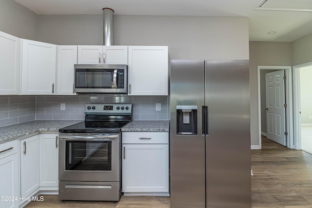 kitchen with white cabinetry, light stone counters, backsplash, appliances with stainless steel finishes, and light wood-type flooring