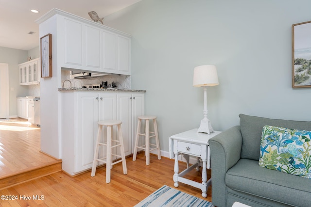 interior space with light hardwood / wood-style flooring, backsplash, light stone countertops, and white cabinets