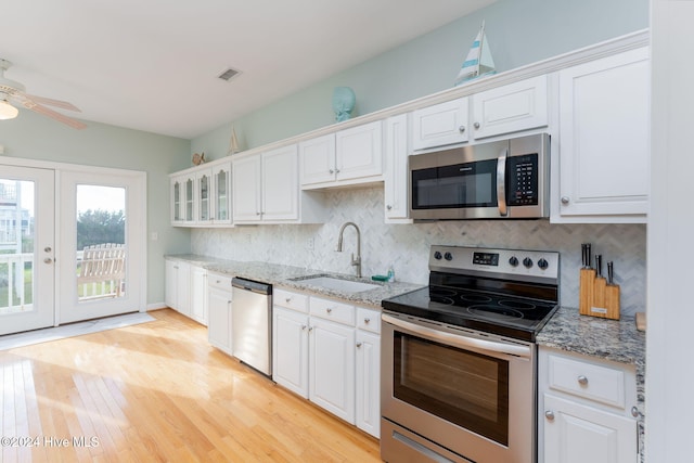 kitchen with stainless steel appliances, white cabinetry, sink, light stone counters, and light wood-type flooring