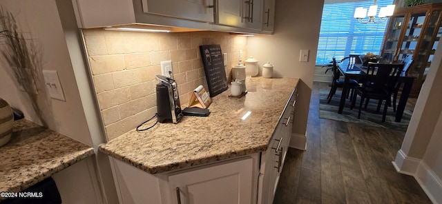 kitchen with light stone counters, a chandelier, dark hardwood / wood-style flooring, pendant lighting, and decorative backsplash