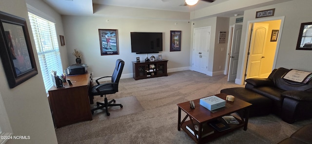 office space featuring light carpet, a tray ceiling, and ceiling fan