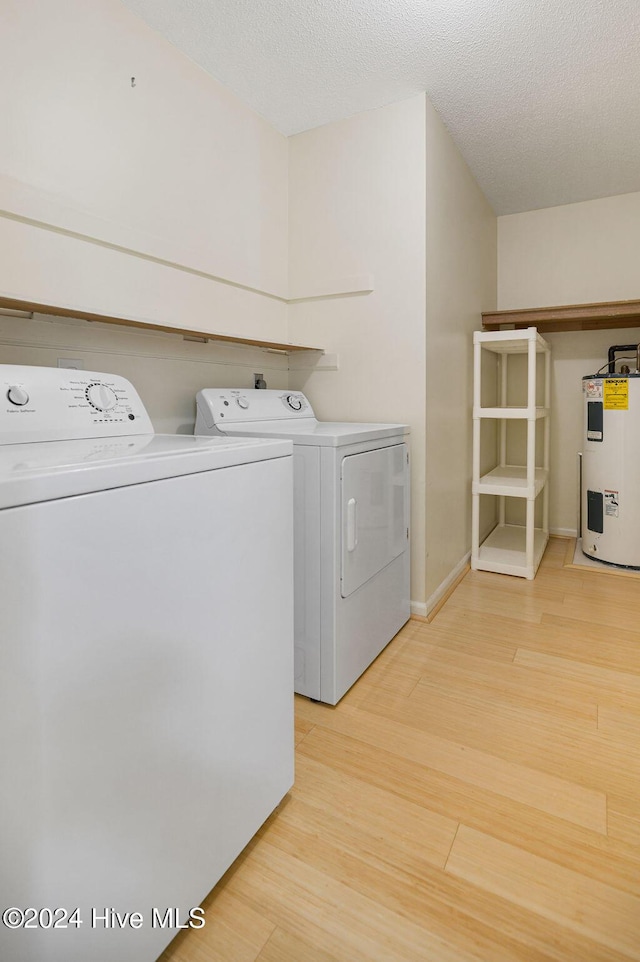 washroom with laundry area, light wood finished floors, a textured ceiling, water heater, and washing machine and dryer