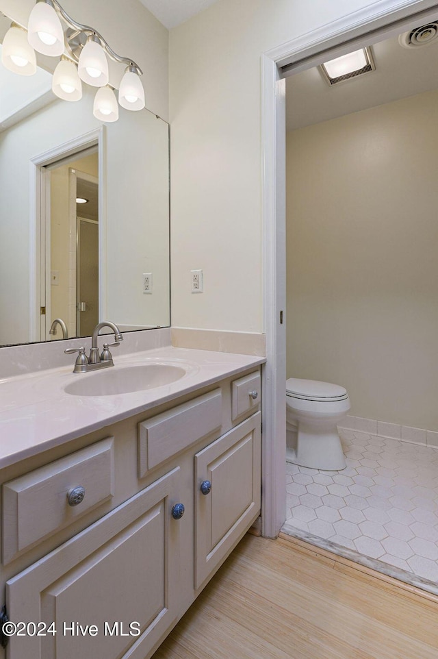 bathroom featuring toilet, wood finished floors, a shower with shower door, and vanity
