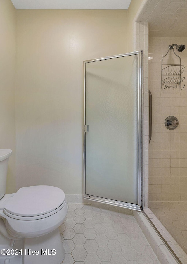 full bath featuring tile patterned floors, toilet, and a shower stall