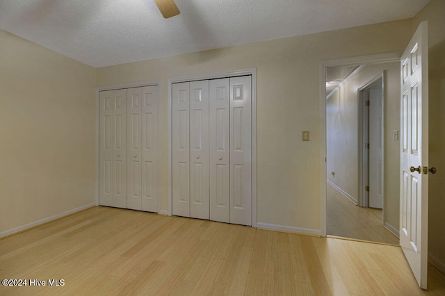 unfurnished bedroom featuring a textured ceiling, two closets, light wood-type flooring, and ceiling fan