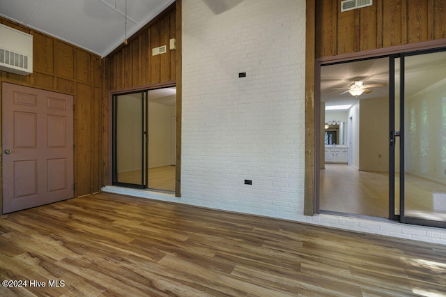 spare room with ceiling fan, hardwood / wood-style flooring, high vaulted ceiling, wood walls, and brick wall