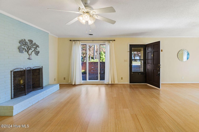 unfurnished living room with ceiling fan, a textured ceiling, light wood-type flooring, a fireplace, and crown molding