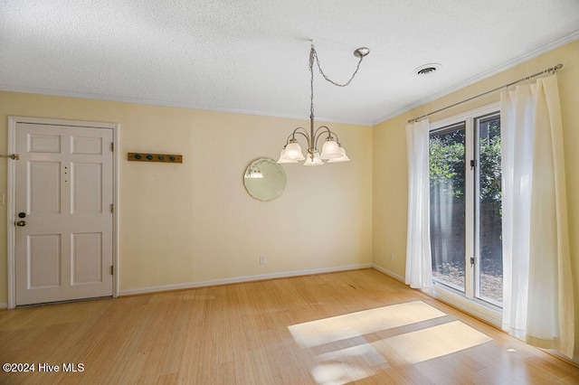 empty room with crown molding, a notable chandelier, a textured ceiling, and light wood-type flooring