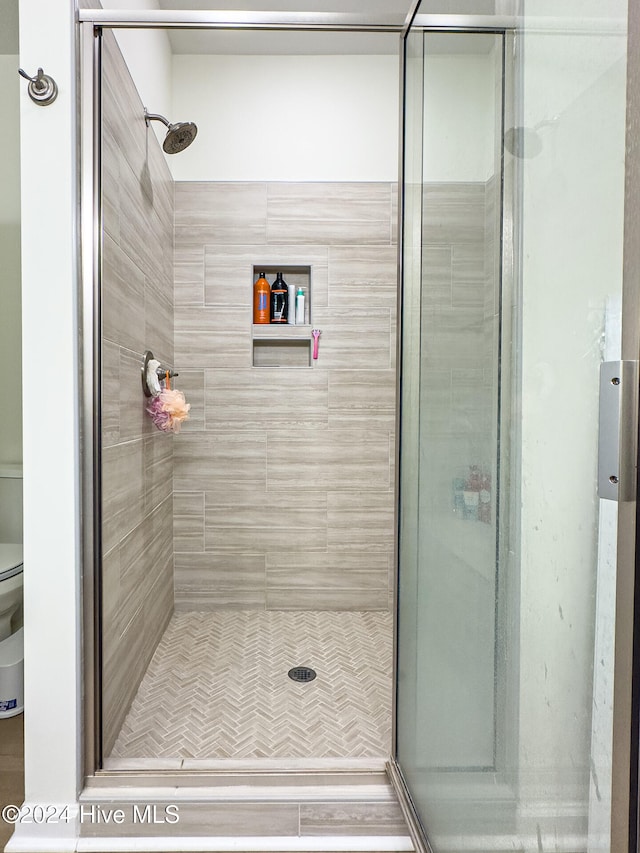 bathroom featuring a shower with door and toilet