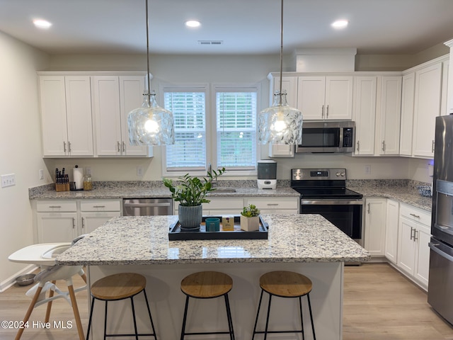 kitchen with appliances with stainless steel finishes, white cabinetry, light hardwood / wood-style flooring, decorative light fixtures, and a center island