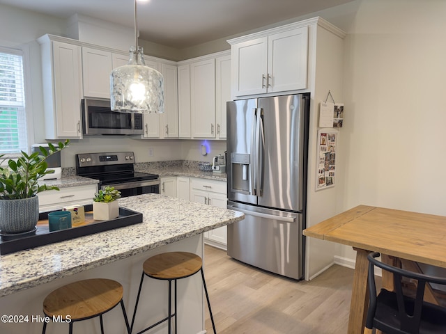 kitchen featuring stainless steel appliances, light stone countertops, pendant lighting, light wood-type flooring, and white cabinetry