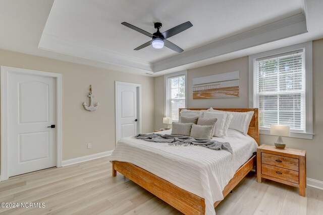 bedroom with an inviting chandelier, ornamental molding, a raised ceiling, and light wood-type flooring