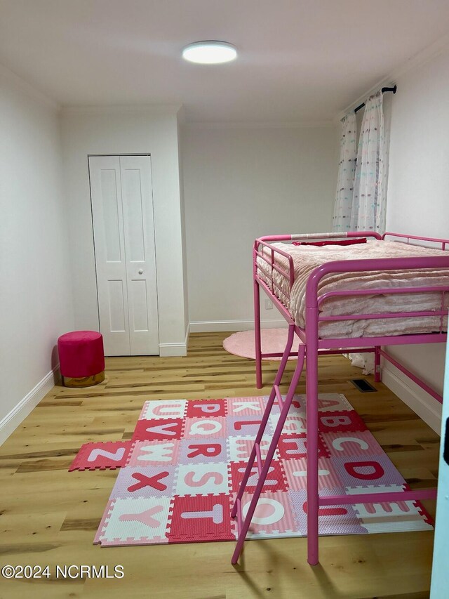 bedroom with hardwood / wood-style floors, crown molding, and a closet