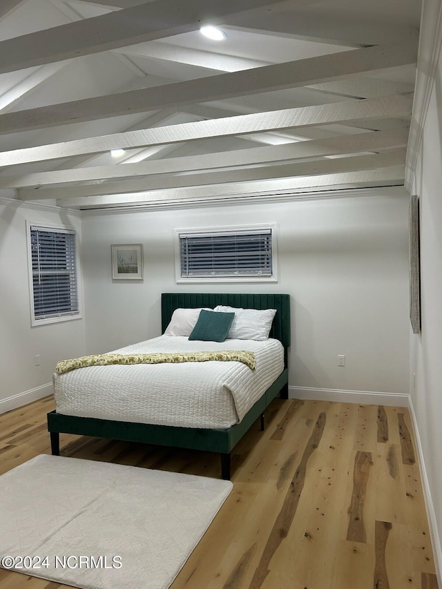 bedroom with baseboards, lofted ceiling with beams, and light wood-style flooring