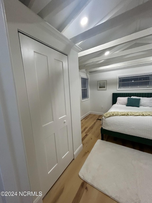 bedroom with light hardwood / wood-style floors, a closet, and beam ceiling