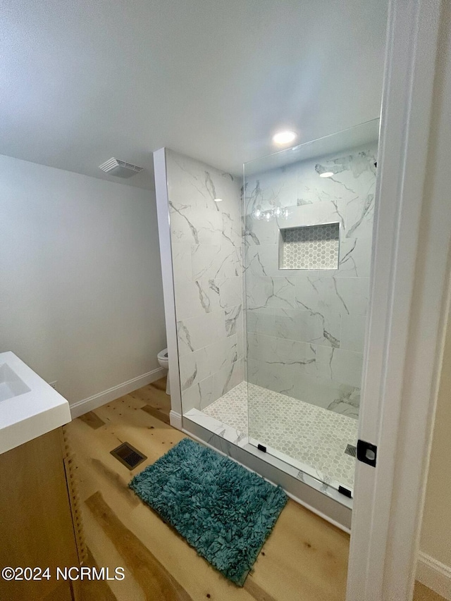 bathroom featuring visible vents, wood finished floors, toilet, baseboards, and a marble finish shower