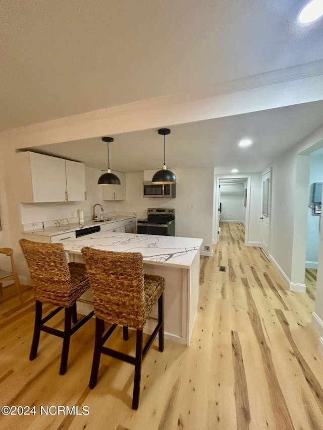 kitchen with light stone countertops, light wood-type flooring, hanging light fixtures, white cabinetry, and stainless steel appliances