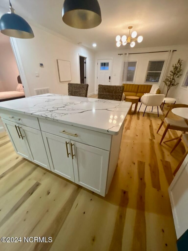 kitchen featuring light hardwood / wood-style floors, white cabinets, light stone countertops, and decorative light fixtures