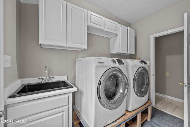 clothes washing area with separate washer and dryer, sink, cabinets, and a textured ceiling