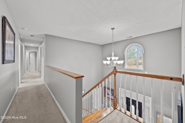 hallway featuring light colored carpet, a textured ceiling, and an inviting chandelier